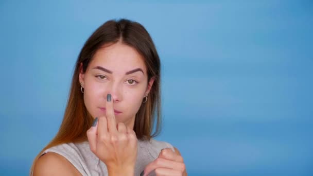 Rolig kvinna i t-shirt leenden, danser, visar långfingret på blå bakgrund — Stockvideo