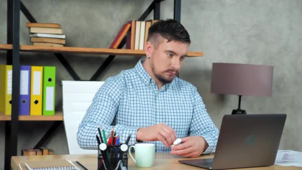 Ofisteki iş adamı kablosuz kulaklık takıyor ve dizüstü bilgisayar kullanmaya başlıyor. — Stok video