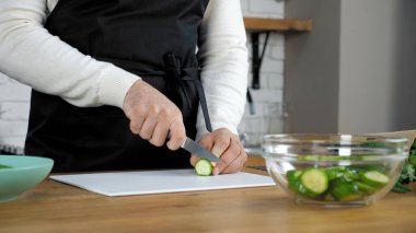 Profesyonel aşçı, siyah önlüklü ev mutfağında taze salatalık dilimledi.