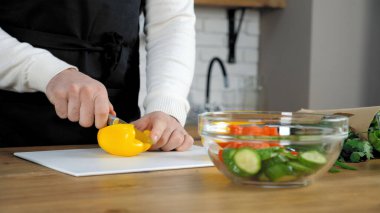 Mutfakta siyah önlüklü aşçı taze sarı biber dilimledi.