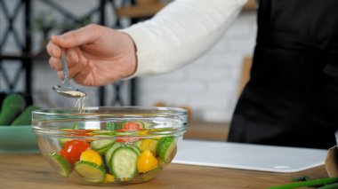 Şef cam kasede pişmiş vejetaryen salatasına susam serpiyor.