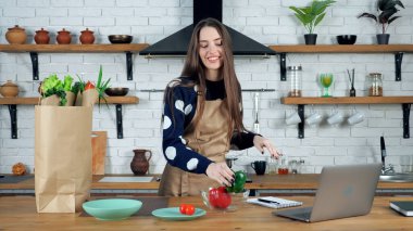 Gülümseyen kadın, kese kağıdından malzemeleri açıyor ve kaseye yeşil dolma biber koyuyor.