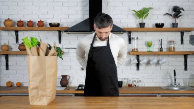 Kazaklı adam mutfağa gelir önlük giyer, aşçıya sağlıklı yemek hazırlar.