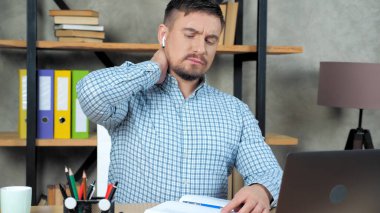 Yorgun iş adamı, uzun bir laptoptan sonra boyun masajı yaparak gergin kaslara masaj yapıyor.