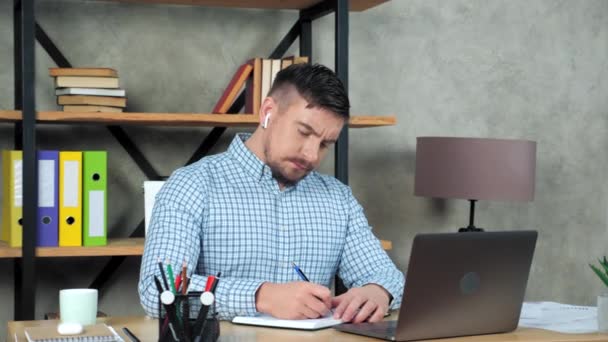 Tired businessman writes in notebook massaging neck after over work at laptop — Stock Video