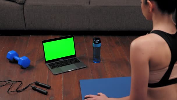 Concepto de ordenador portátil de pantalla verde: Mujer atlética en ropa deportiva se sienta en la esterilla de yoga — Vídeos de Stock