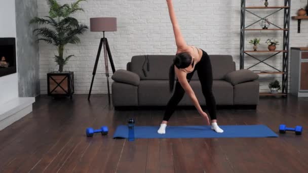 Mujer joven en forma en ropa deportiva haciendo calentamiento antes del entrenamiento en esterilla de yoga en casa — Vídeos de Stock