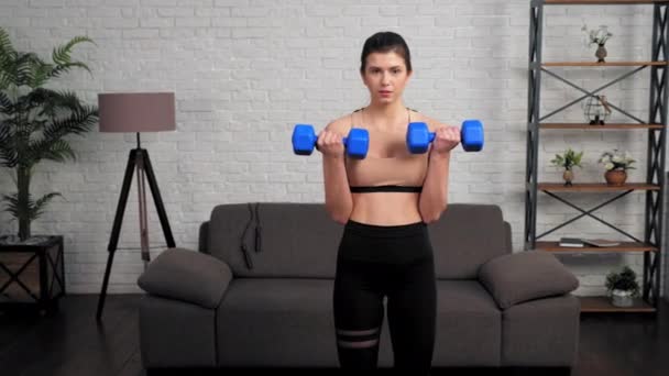 Спортивная женщина делает бицепсы с гантелями, тренировки дома в спальне — стоковое видео