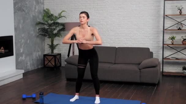 Młoda kobieta w odzieży sportowej robi rozgrzewkę przed treningiem na macie do jogi w domu — Wideo stockowe