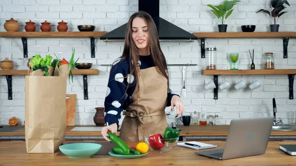 Glimlachende vrouw huisvrouw pakt ingrediënten uit papieren zak zet komkommer op kom — Stockfoto