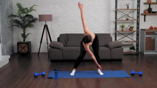 Mujer joven en forma en ropa deportiva haciendo calentamiento antes del entrenamiento en esterilla de yoga en casa — Vídeos de Stock