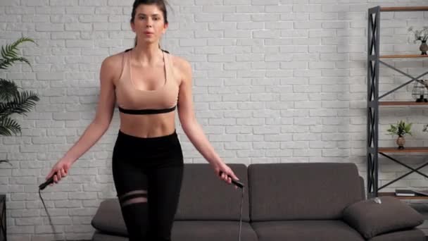 Sportowa muskularna kobieta w odzieży sportowej ćwiczy skakankę w domu — Wideo stockowe