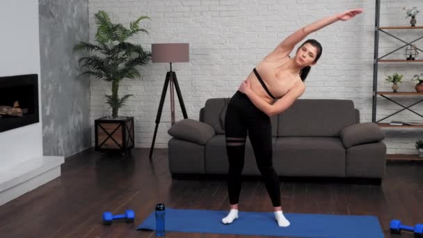 Mujer joven en forma en ropa deportiva haciendo calentamiento antes del entrenamiento en esterilla de yoga en casa — Vídeos de Stock