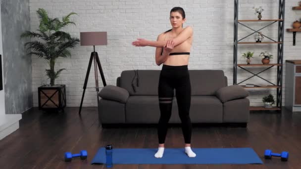 Молодая женщина в спортивной одежде перед тренировкой на коврике для йоги дома — стоковое видео