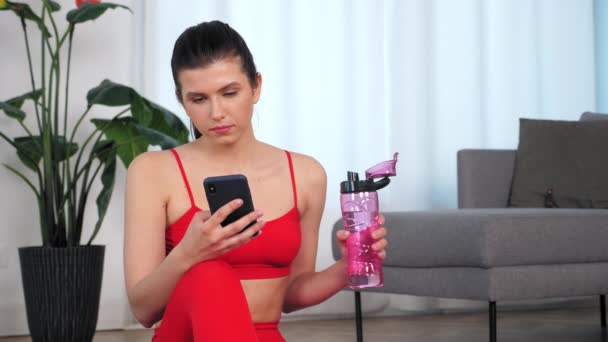 Mujer deportiva utiliza el teléfono inteligente beber agua después de ejercicio de fitness activo ejercicio — Vídeos de Stock