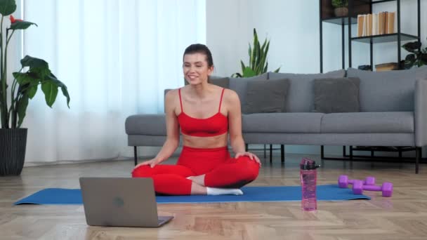 Fit bir kadın yoga minderinde oturur fitness eğitmenine internetten bilgisayar araması yapmasını söyler. — Stok video