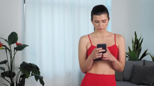 Portret atletyczny fit fitness kobieta używa smartfona w domu w salonie — Wideo stockowe