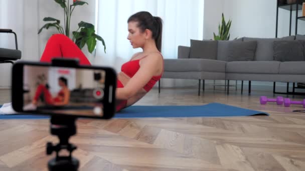 女性健身博主一边躺在垫子上一边教运动，一边教健美操 — 图库视频影像