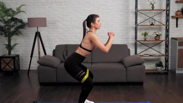 Vacker atletisk muskulös flicka idrottskvinna gör squat motion med loop band — Stockvideo