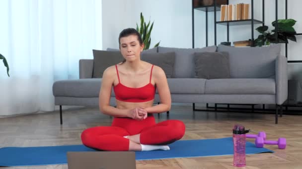 Камера зум в женщине сидит на коврике йоги слушать разговоры фитнес-тренер, учиться онлайн — стоковое видео