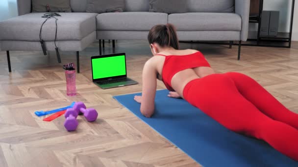 Mujer fuerte fitness haciendo tablón en estera de yoga mirando pantalla verde pantalla portátil — Vídeo de stock