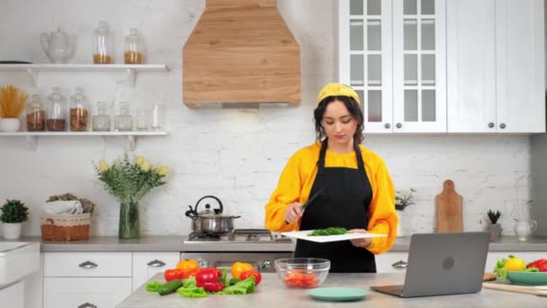 Vrouw in keukenmessen gesneden komkommer van snijplank in glazen salade kom — Stockvideo