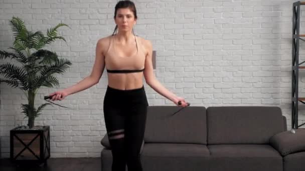 Спортивная мускулистая женщина в спортивной форме делает упражнения на скакалке дома — стоковое видео