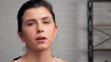 Atletik kaslı, yorgun kadın oturma odasında kameraya bakıyor.