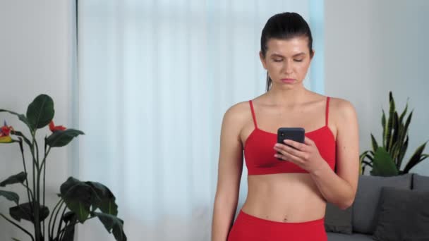 Retrato serio atlético fitness mujer utiliza smartphone levanta la cabeza mira cámara — Vídeos de Stock