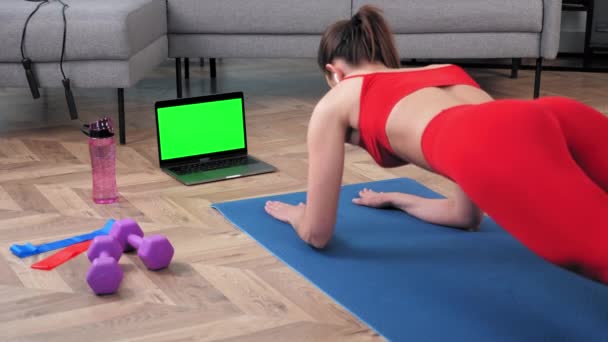 Green-Screen-Laptop: Starke Fitness-Frau macht Brettgymnastik auf Yoga-blauer Matte — Stockvideo