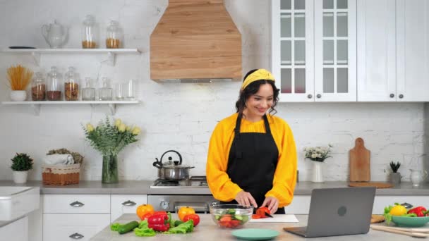 ホームキッチンスライスで笑う女性トマトリッスンシェフ、勉強オンラインラップトップ — ストック動画
