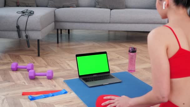 Woman sits on mat looks laptop display, tells listen fitness trainer video call — Stockvideo