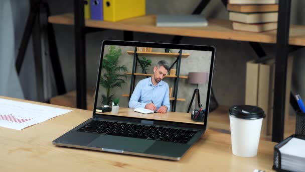 Laptop staat op tafel display met zakenman in kantoor schrijft in notebook — Stockvideo