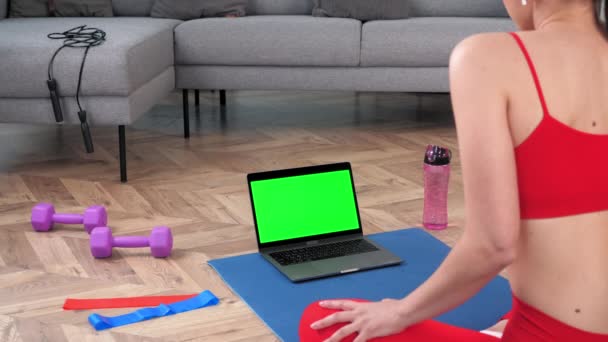 Portátil de pantalla verde: Mujer fitness se sienta en la esterilla de yoga haciendo calentamiento antes del entrenamiento — Vídeo de stock