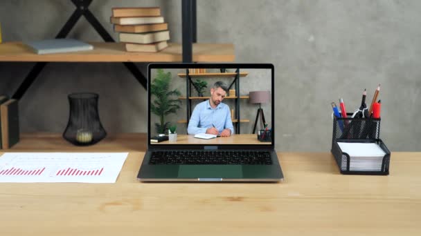 Laptop staat op tafel display met zakenman in kantoor schrijft in notebook — Stockvideo