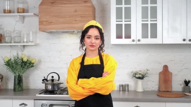 Портрет серьезная домохозяйка скрещивая руки глядя в камеру в доме современной кухни — стоковое видео