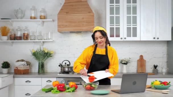 Усміхнена жінка в кухонних ножах нарізала помідор з ріжучої дошки в салатну миску — стокове відео