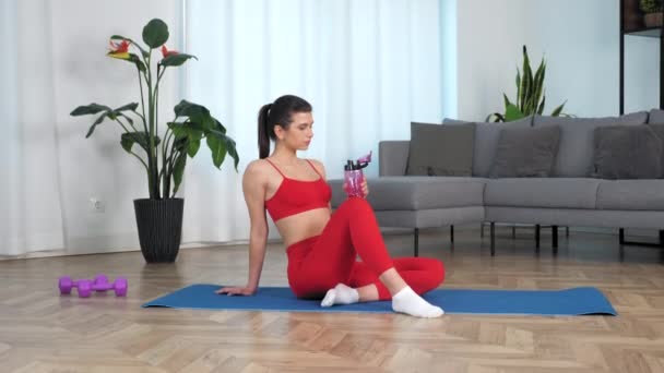 Pasuje piękna kobieta siedzi na macie fitness jogi trzymając butelkę wody w ręku — Wideo stockowe