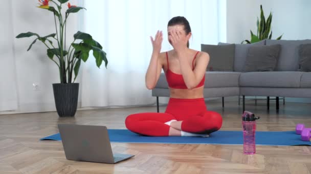 Спортивна усміхнена жінка в спортивному одязі, що сидить на килимку для йоги вдома у вітальні — стокове відео