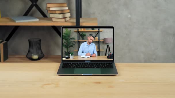 Laptop staat op een lege tafel monitor met zakenman schrijft in notebook — Stockvideo
