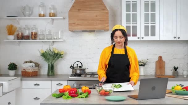 Kvinna i kök knivar skivad gurka från skärbräda i glas sallad skål — Stockvideo