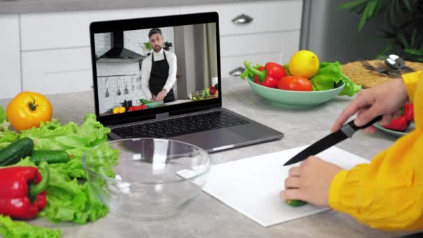 Woman in kitchen study online video call laptop listen chef slices cucumber — Stock Video