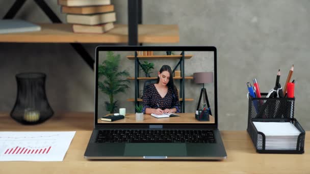 Ноутбук стоїть на дисплеї стола з бізнес-леді в офісі пише в блокноті — стокове відео