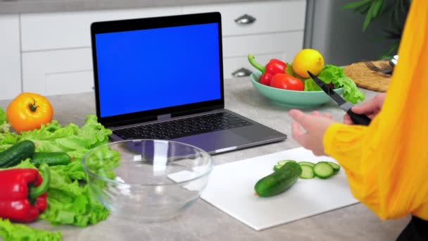Kék képernyős laptop: nő háziasszony a konyhában azt mondja figyelj séf szeletek uborka — Stock videók