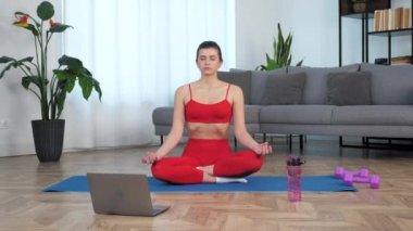 Güzel, formda bir kız, Lotus pozisyonunda meditasyon yaparken spor spreyi mavi minder üzerinde oturur.