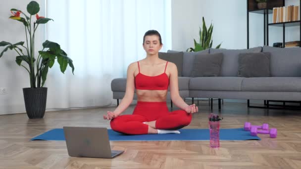 Hermosa chica en forma se sienta a meditar en posición de loto en el deporte de fitness alfombra azul — Vídeo de stock