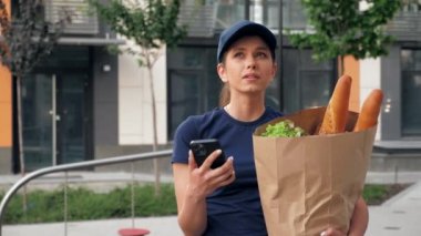 Yemek teslimatçısı kadın kurye akıllı telefon, kağıt torba görünümlü adres kullanıyor.