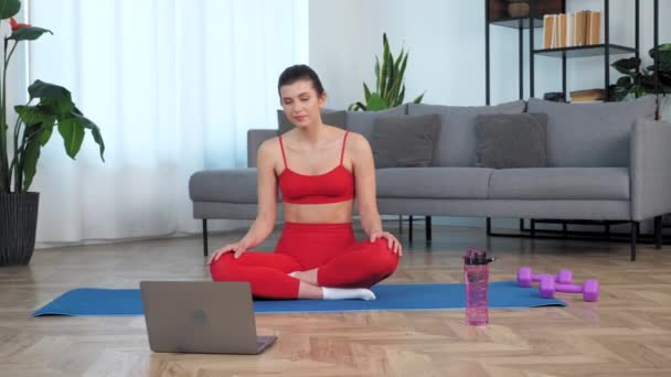 Mujer sonriente en forma se sienta en estera de yoga ver curso de educación deportiva a distancia — Vídeo de stock