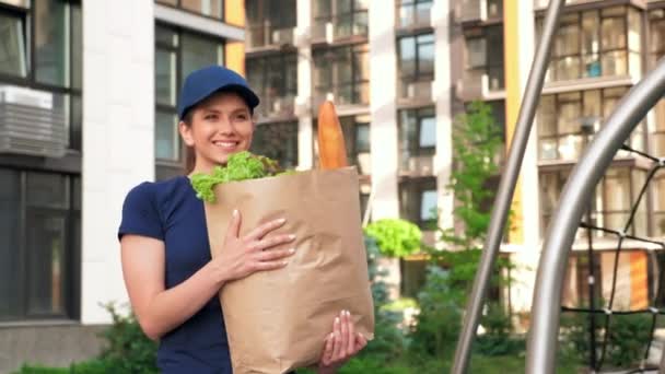 Correio sorridente da mulher da entrega com mantimentos do saco de papel para entregar o cliente da ordem — Vídeo de Stock