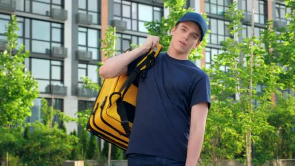 Retrato jovem mensageiro entrega de alimentos coloca em mochila térmica parece câmera — Vídeo de Stock